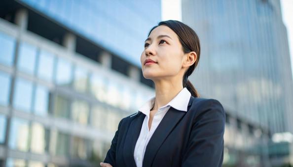 高層ビル背景にスーツの女性が空を見つめる 高層ビル背景にスーツの女性が空を見つめるの写真