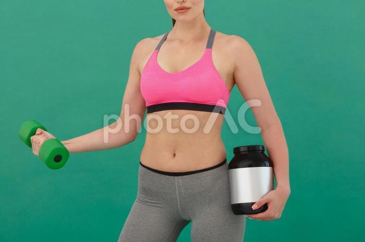 プロテインの容器を持ちながらダンベル運動する女性（緑背景） シェイプアップ,ダイエット,女性の写真素材