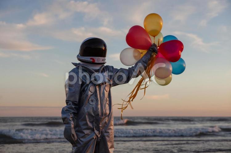 夕焼けをバックに風船を掲げる宇宙服の人 宇宙人,宇宙服,人物の写真素材