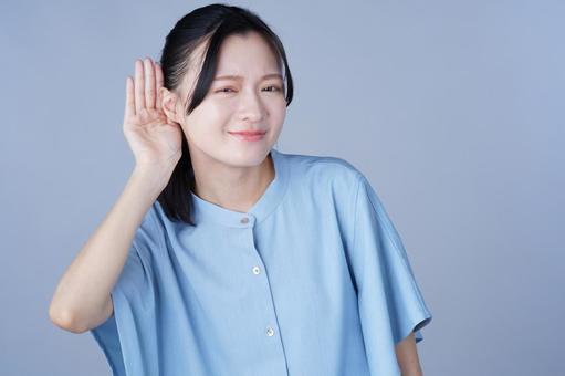 耳に手を当てた青い服の女性の写真