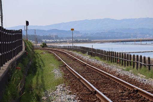 海岸沿いの線路のレールと港町と山並みと空の写真
