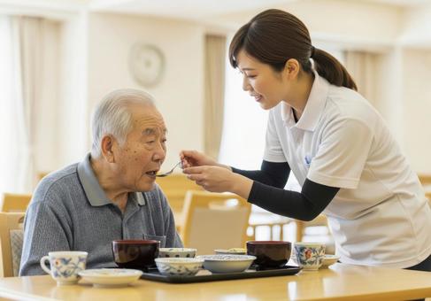女性介護士が高齢男性に食事介助する場面 女性介護士が高齢男性に食事介助する場面の写真