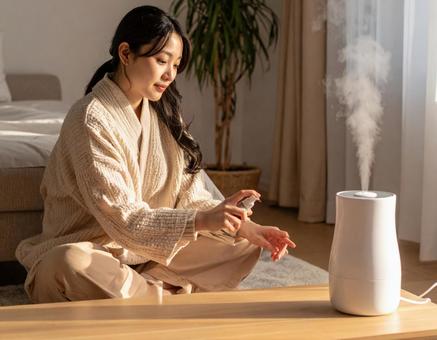 加湿器のそばでスキンケアをする女性 加湿器のそばでスキンケアをする女性の写真