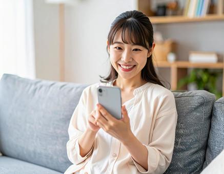 自宅でスマホを操作する若い女性 自宅でスマホを操作する若い女性の写真