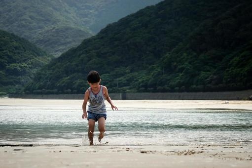 <素材>夕暮れの海で水遊びをする男の子 <素材>夕暮れの海で水遊びをする男の子の写真