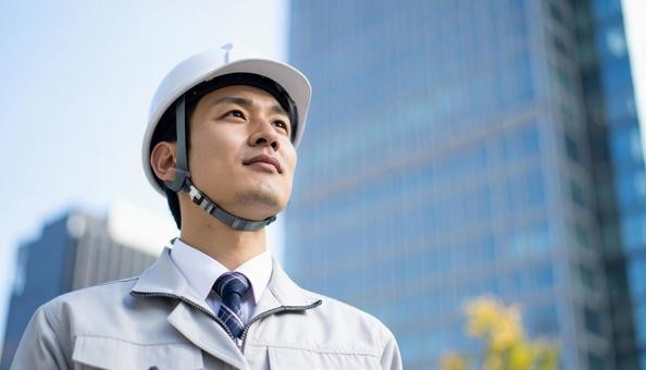 高層ビルの斜め上を見つめる若い作業服男性 高層ビルの斜め上を見つめる若い作業服男性の写真