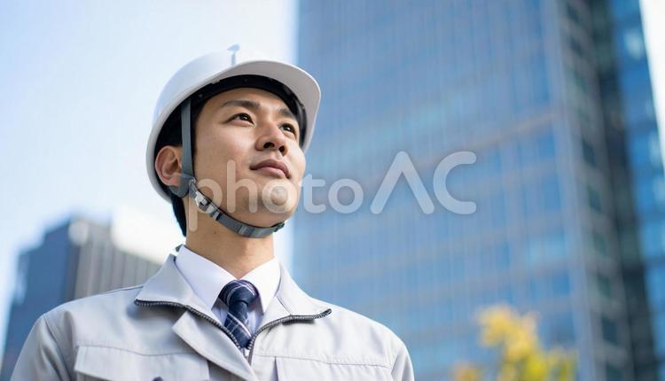 高層ビルの斜め上を見つめる若い作業服男性 男性,社会人,30代の写真素材
