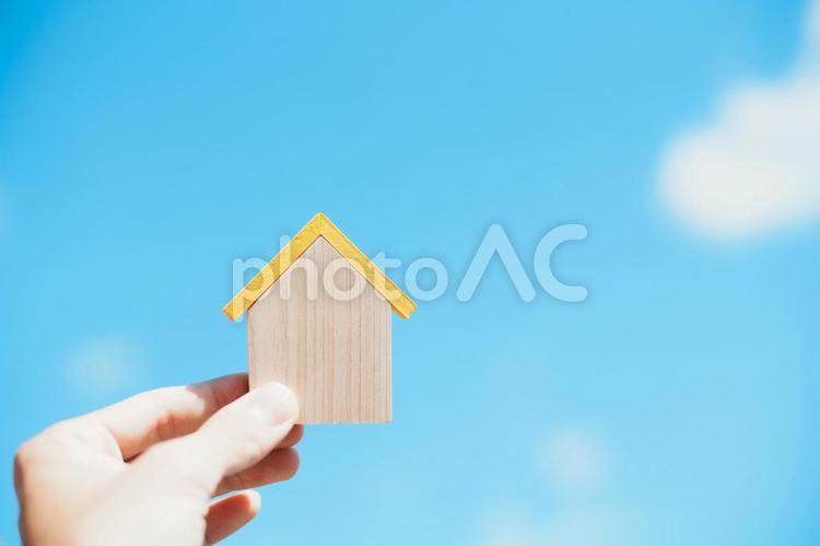 小さな木製の家を持つ人の手元と青空背景 家,住宅,青空の写真素材