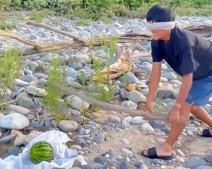 A man splitting a watermelon on the riverbank, JPG