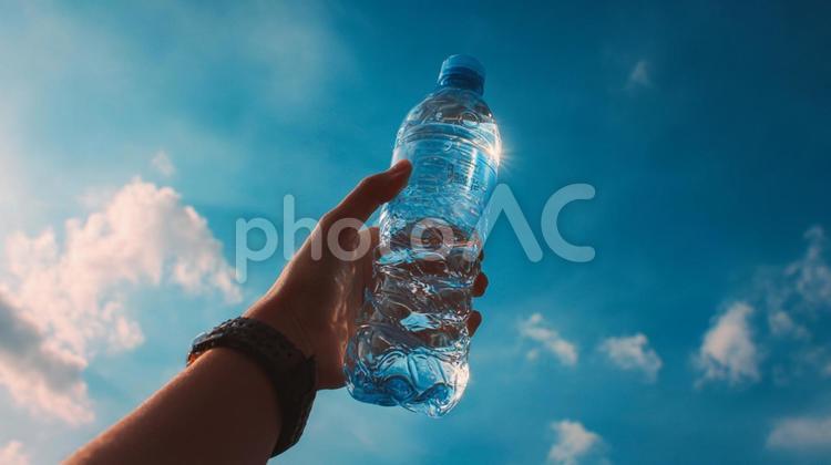 青空に掲げられたペットボトルの水 ペットボトル,水,手の写真素材