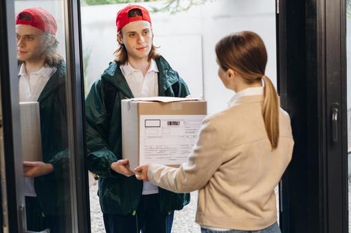 玄関で段ボール箱を女性に渡す配達員の男性 配達,フードデリバリー,デリバリーの写真素材