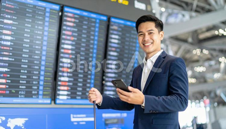 空港で携帯と荷物を持つビジネスマン ビジネスマン,商社マン,スマホの写真素材