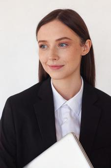 パソコンを持ち横を見て微笑む外国人女性の写真