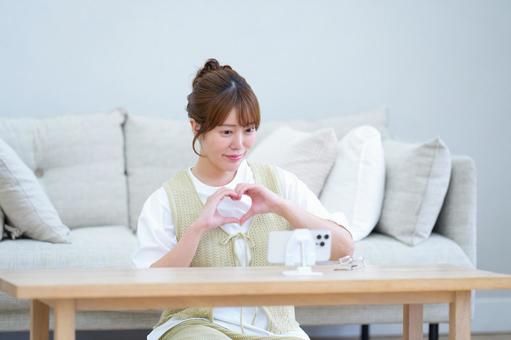 スマホに手ハートをする女性の写真