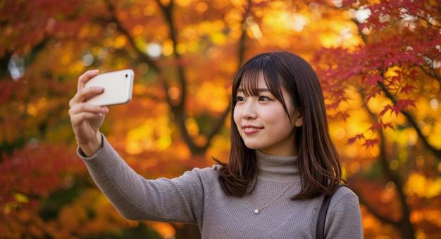 紅葉 深紅の楓を背景に自撮りする若い女性 紅葉 深紅の楓を背景に自撮りする若い女性の写真