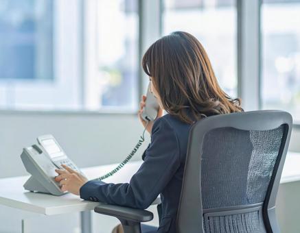 オフィスで内線電話に出る女性の写真
