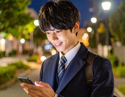 笑顔でスマホを操作する男子高校生 笑顔でスマホを操作する男子高校生の写真