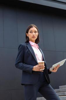 コーヒーとタブレットを持ってオフィスビルの外の階段を登るビジネスウーマン ビジネスウーマン,ビジネス,女性の写真素材