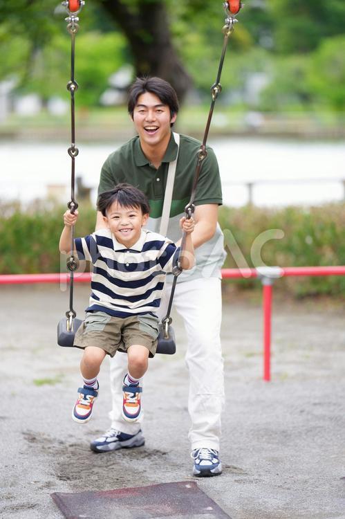 ブランコに乗る息子を押す笑顔の父 親子,ブランコ,乗るの写真素材