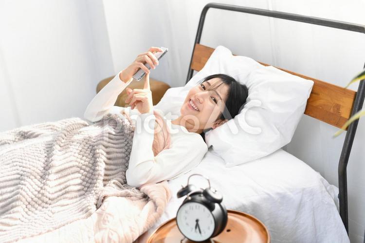 ベッドでスマホを持つ笑顔のアジア人女性 ベッド,スマートフォン,女性の写真素材