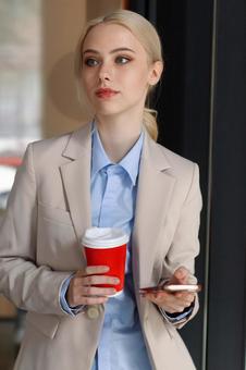 コーヒーとスマートフォンを持って立つビジネスウーマン ビジネスウーマン,ビジネス,女性の写真素材