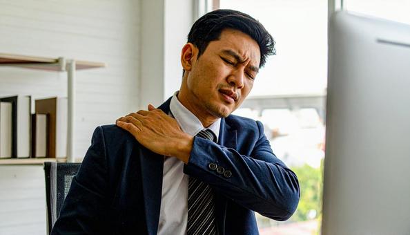 デスクワークで肩を回しほぐすビジネスマンの写真