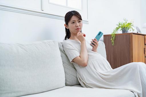 ソファで携帯を持つ女性 悩む,妊婦,妊娠の写真素材