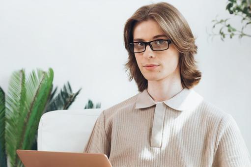 リビングでノートパソコンを使うカメラ目線の若い男性 男性,外国人,欧米人の写真素材