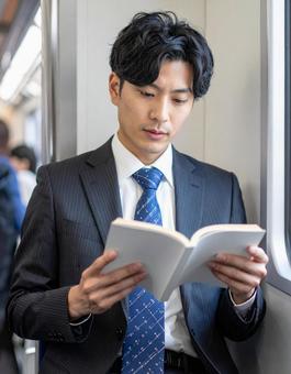 電車の中で本を読むビジネスマン男性の写真