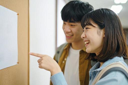 掲示板を見ながら談笑する大学生カップル 掲示板を見ながら談笑する大学生カップルの写真