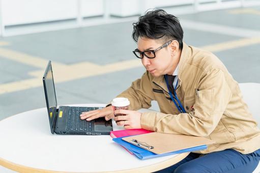 ドリンクを持ちながら仕事する作業服の男性 ドリンクを持ちながら仕事する作業服の男性 ビジネス,ビジネスマン,作業員の写真素材