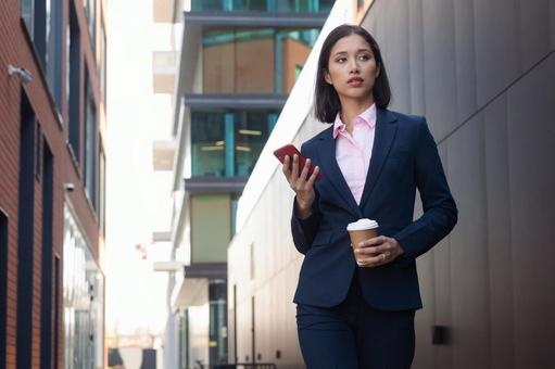 街なかでコーヒーとスマートフォンを持って立っているアジア人ビジネスウーマン ビジネスウーマン,ビジネス,女性の写真素材