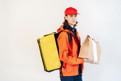 紙袋を持つカメラ目線のフードデリバリーの男性（白背景）の写真