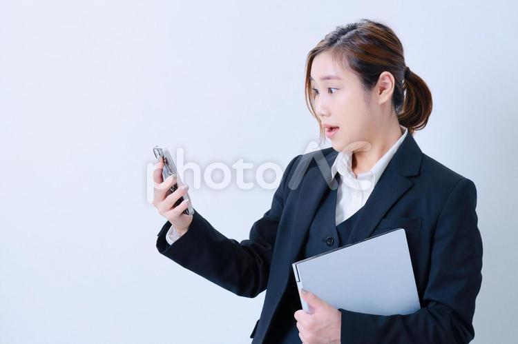 携帯を見て驚きの表情をするスーツ姿の女性 女性,スマホ,驚くの写真素材