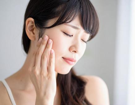 困った顔で手を頬に当てる若い女性の写真