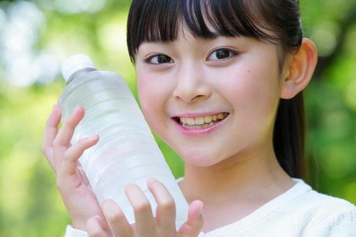 公園で水のペットボトルを頬に当てている女の子 子ども,女の子,小学生の写真素材
