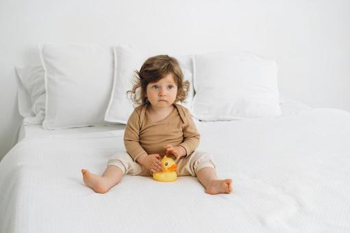 ベッドの上でお座りする赤ちゃんとアヒルの玩具 ベッドの上でお座りする赤ちゃんとアヒルの玩具 赤ちゃん,かわいい,お座りの写真素材