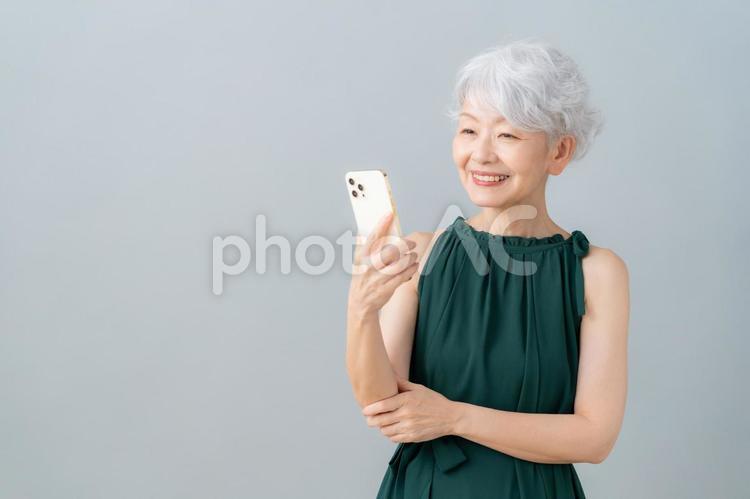 グレーバックでスマホを見るシニア女性 女性,スマホ,シニアの写真素材