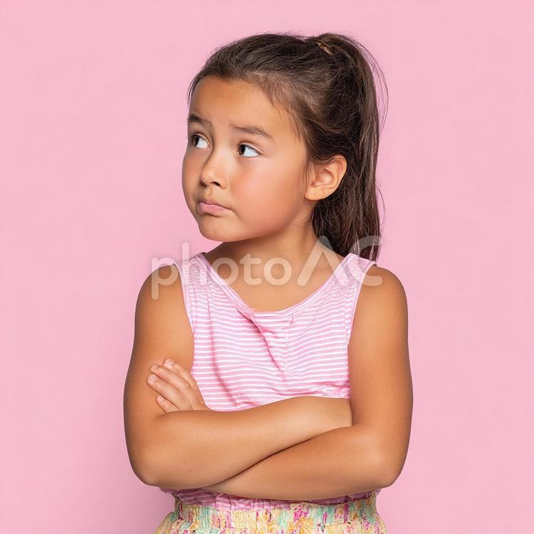 ピンクの背景に立つ、拗ねた様子の幼い少女 女の子,子供,幼女の写真素材