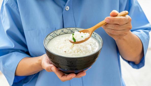 白いお粥を木の匙で掬って差し出す女性の手 白いお粥を木の匙で掬って差し出す女性の手の写真