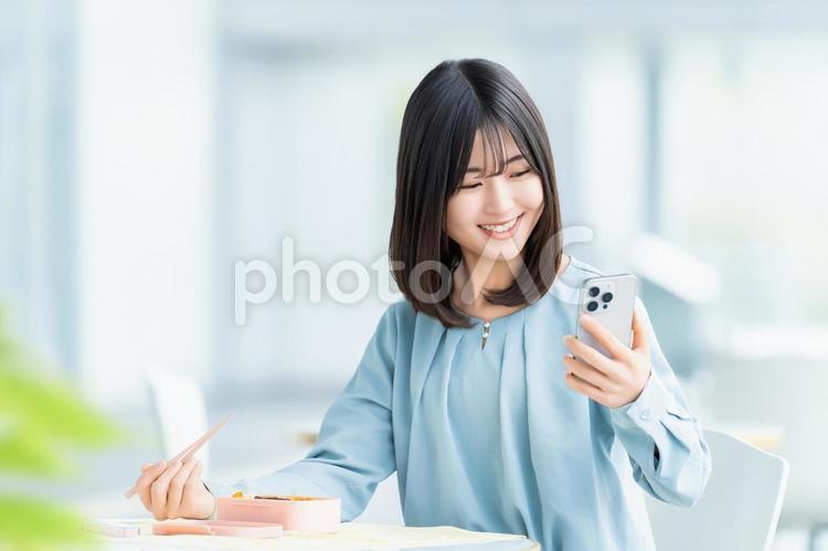 スマホを見ながらお弁当を食べる女性 女性,お弁当,ランチの写真素材