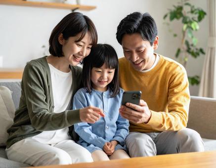 リビングでスマホを仲良く操作する家族の写真