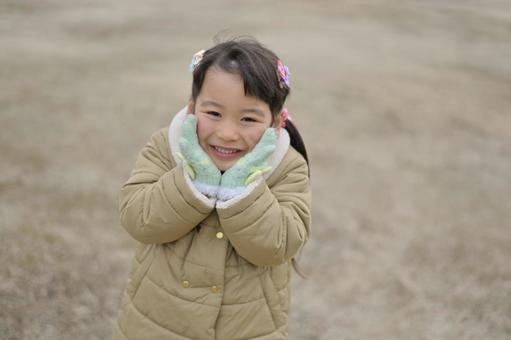 A smiling girl wrapping her cheeks in gloves, JPG