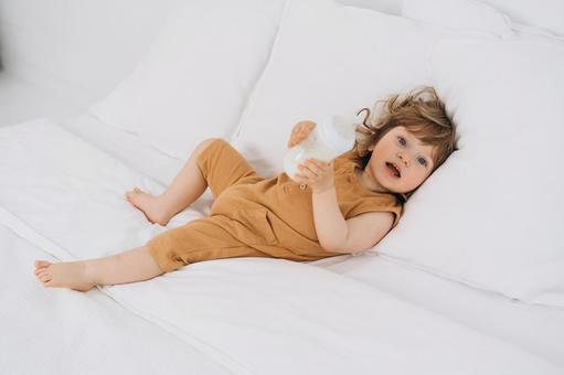 ベッドで哺乳瓶を持ちカメラ目線の子供 ベッドで哺乳瓶を持ちカメラ目線の子供 赤ちゃん,哺乳瓶,ミルクの写真素材