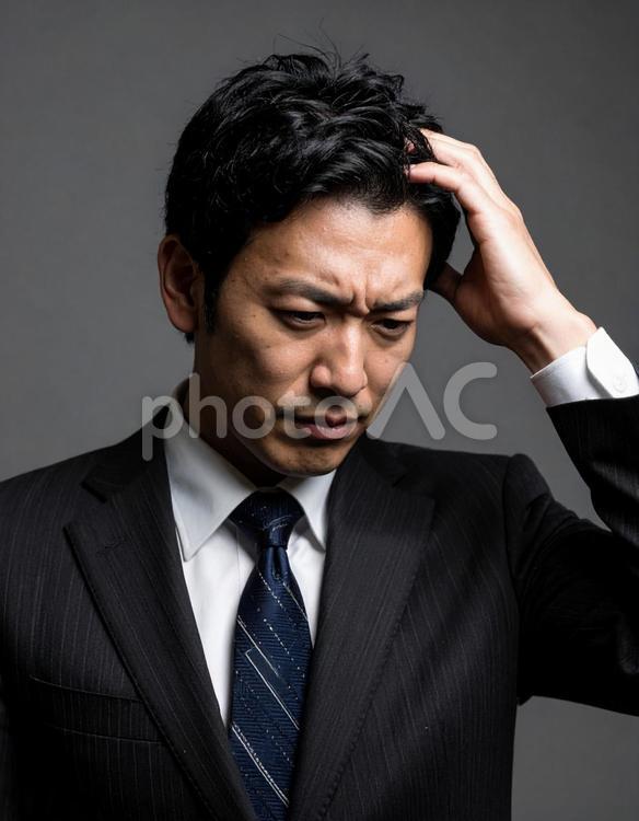 頭を抱えるスーツ姿の日本人男性 ビジネスマン,悩む,頭を抱えるの写真素材