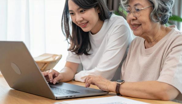 家族にパソコン操作を教わるシニア女性の写真
