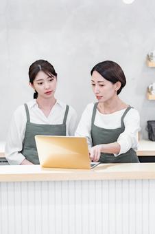 パソコンを見るエプロンをつけた女性 pc,パソコン,二人の写真素材