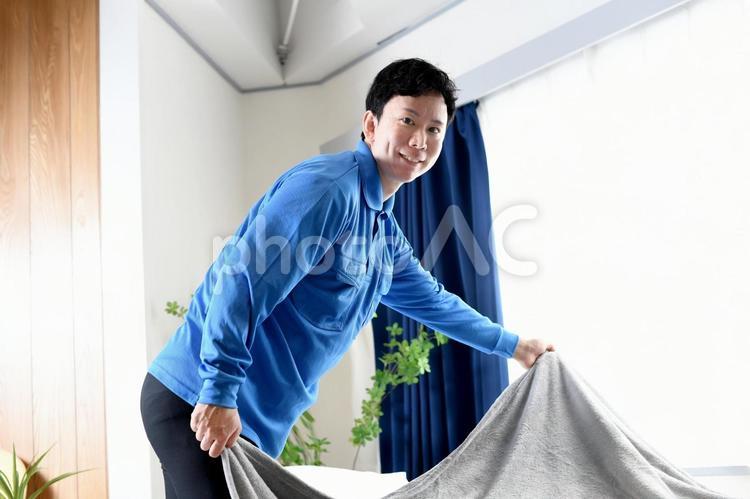 ベッドメイキングする作業着のアジア人男性 ベッドメイキング,ベッド,ベッドメイクの写真素材