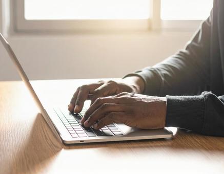 木製の机の上でノートパソコンを使う人物の写真