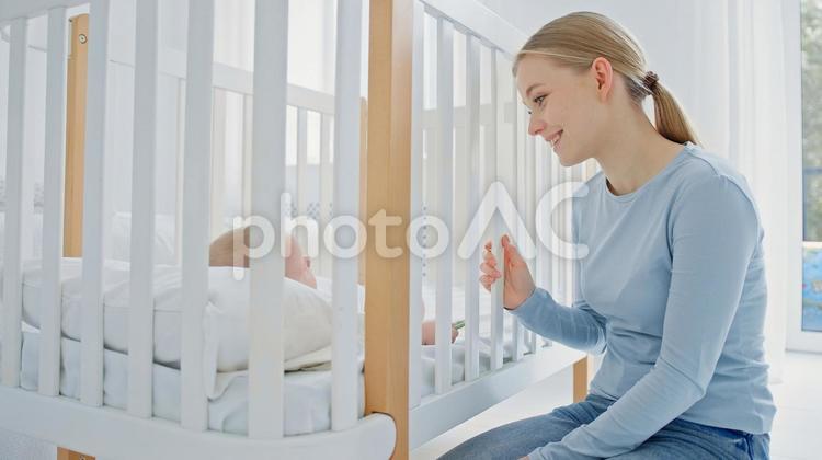 ベッドの横に座り笑顔で赤ちゃんを見ている母 女性,ベビーベッド,見つめるの写真素材